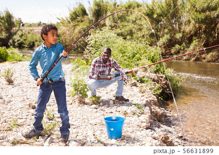 Boy pulling fish from river 56631899