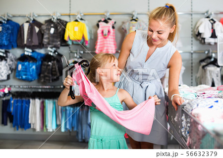 Female with girl choosing different clothes in the dress shop Female with girl choosing different clothes in the dress shop 56632379