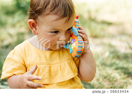 Curious little girl using toy phone outdoors in summer day. Gen z Curious little girl using toy phone outdoors in summer day. Gen z 56633434