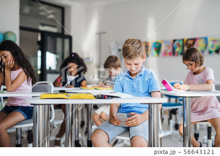 A small school boy with smartphone sitting at the desk in classroom, playing. 56643121