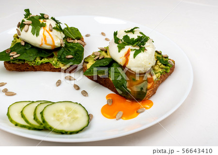 Poached eggs with avocado, spinach leaves and seeds on toasts bread on a white plate on the white 56643410