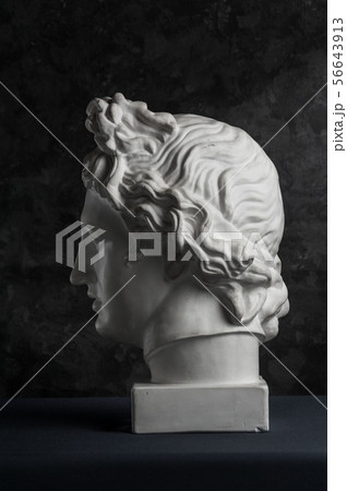 Gypsum copy of ancient statue Apollo head on dark textured background. Plaster sculpture man face. 56643913