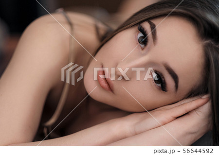 Beautiful brunette girl with brown eyes with bare shoulders lying on the bed. Face close up. Asian 56644592