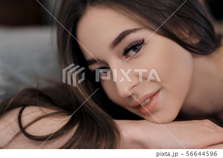Beautiful brunette girl with brown eyes with bare shoulders lying on the bed. Face close up. Asian Beautiful brunette girl with brown eyes with bare shoulders lying on the bed. Face close up. Asian 56644596