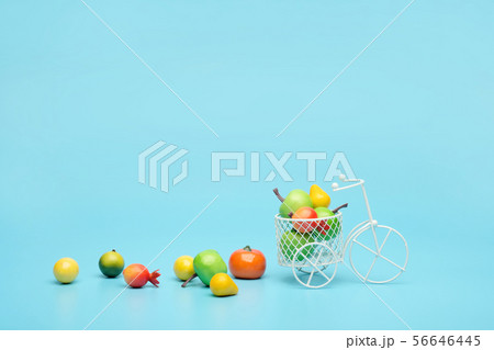 White wire bicycle with a basket filled with mini fruit. Near the bucket with vegetables and fruits 56646445