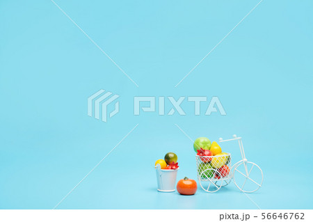 White wire bicycle with a basket filled with mini fruit. Near the bucket with vegetables and fruits White wire bicycle with a basket filled with mini fruit. Near the bucket with vegetables and fruits 56646762