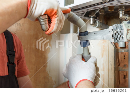 The workers is soldering  the gas boiler pipes. 56656261