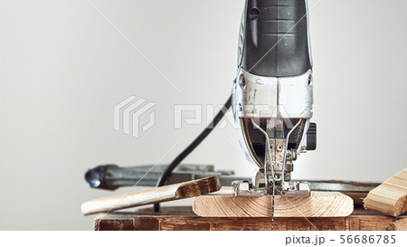 Electric jigsaw closeup and wood boards on a Board on a gray background. Front view. Electric jigsaw closeup and wood boards on a Board on a gray background. Front view. 56686785