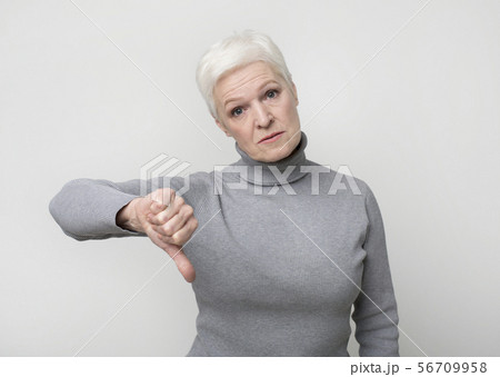 Upset senior woman showing thumb down gesture as rejection symbol Upset senior woman showing thumb down gesture as rejection symbol 56709958