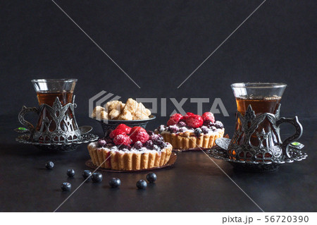 Tea cups, tarts cakes sweets on black background Tea cups, tarts cakes sweets on black background 56720390