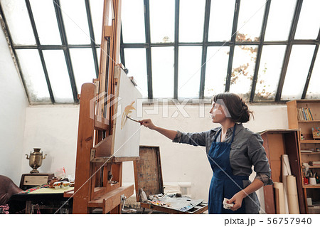 Young beautiful woman painter among easels and canvases in a bright studio. 56757940