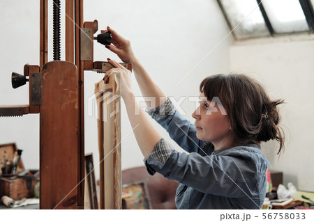 Woman artist fastens a canvas on a large wooden easel. Woman artist fastens a canvas on a large wooden easel. 56758033