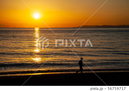 夕日の砂浜を走る人のシルエットの写真素材