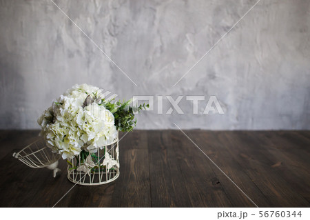 White flowers in a white cage stand on a wooden floor on a gray background 56760344