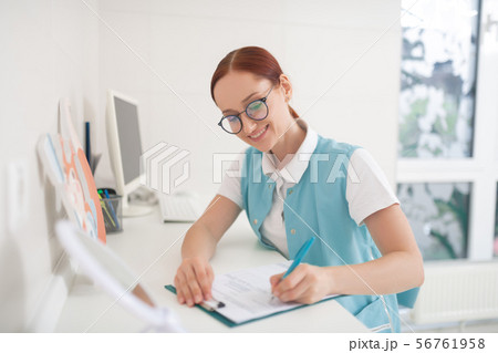 Red-haired dentist wearing glasses filling in some form 56761958