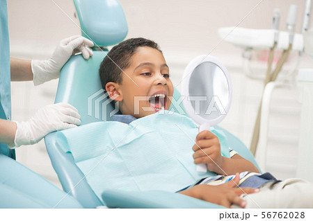 Boy opening mouth and looking into mirror while visiting dentist Boy opening mouth and looking into mirror while visiting dentist 56762028
