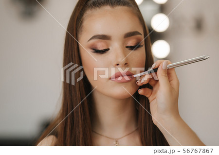 Makeup artist applies lipstick. Hand of make-up master, painting lips of young beauty redhead model Makeup artist applies lipstick. Hand of make-up master, painting lips of young beauty redhead model 56767867
