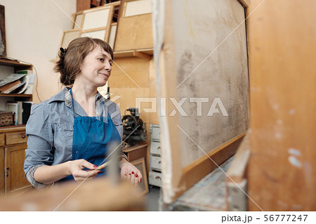 Young beautiful woman painter among easels and canvases in a bright studio. Young beautiful woman painter among easels and canvases in a bright studio. 56777247