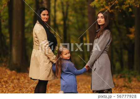 Mom and two daughter have fun in ther park. Youngest daughter collect leaves and smile. Happy family 56777928