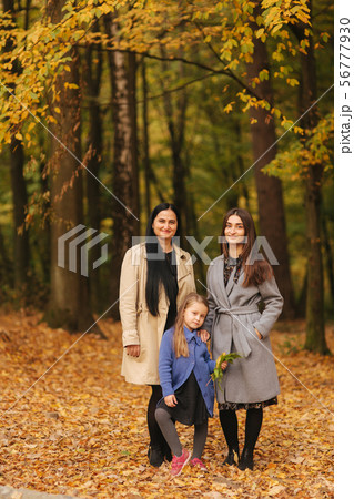 Mom and two daughter have fun in ther park. Youngest daughter collect leaves and smile. Happy family 56777930