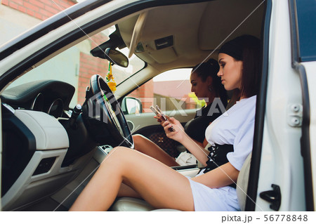 Beautiful woman smiling while sitting on the passenger seats in the car. Girl is using a smartphone. 56778848