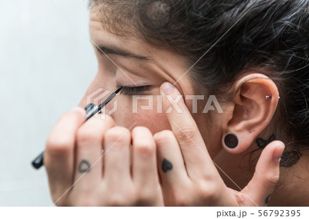 Young woman applies eyeliner to her eye in the bathroom. 56792395