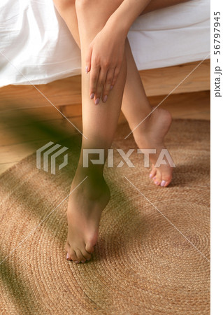 Young woman sitting on bed and touching her leg Young woman sitting on bed and touching her leg 56797945