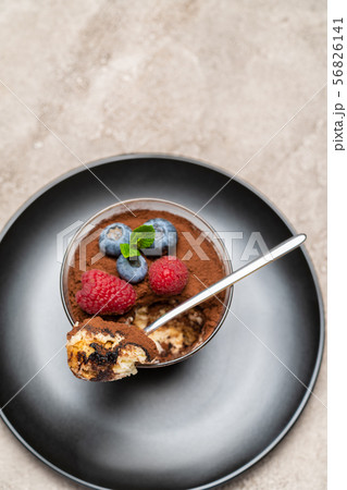 Classic tiramisu dessert portion with blueberries and raspberries in a glass cup on concrete Classic tiramisu dessert portion with blueberries and raspberries in a glass cup on concrete 56826141