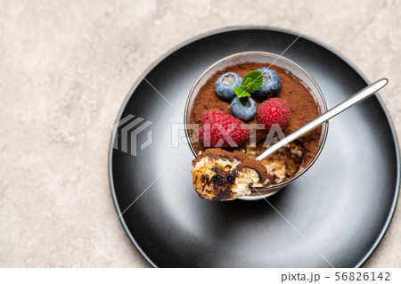 Classic tiramisu dessert portion with blueberries and raspberries in a glass cup on concrete Classic tiramisu dessert portion with blueberries and raspberries in a glass cup on concrete 56826142
