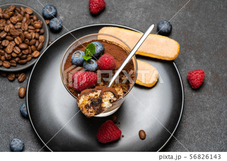 Classic tiramisu dessert portion with blueberries and raspberries in a glass cup on stone serving 56826143