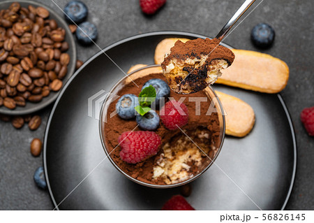 Classic tiramisu dessert portion with blueberries and raspberries in a glass cup on stone serving Classic tiramisu dessert portion with blueberries and raspberries in a glass cup on stone serving 56826145