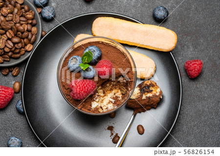 Classic tiramisu dessert portion with blueberries and raspberries in a glass cup on stone serving 56826154