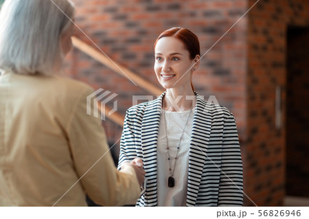 Young red-haired businesswoman shaking hands with her senior colleague Young red-haired businesswoman shaking hands with her senior colleague 56826946