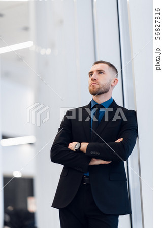 Middle-aged man standing with folded arms leaning against a windowsill turning to look at the camera 56827316