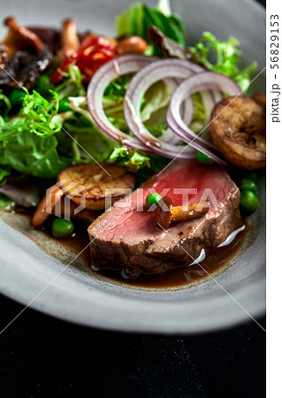 beef tagliata with vegetables. Close-up, low key, gray background. 56829153