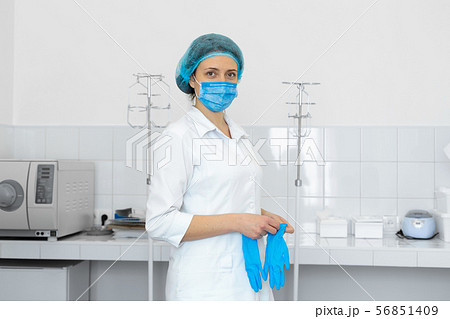 Nurse in scrub and mask puts gloves on her hands Nurse in scrub and mask puts gloves on her hands 56851409