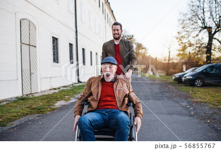 Young man and his senior father in wheelchair on a walk in town, having fun. 56855767
