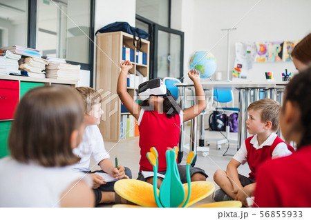 A group of small school kids with VR goggles sitting on the floor in class. 56855933