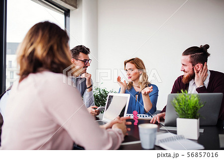 A group of young business people with laptop sitting in an office, talking. A group of young business people with laptop sitting in an office, talking. 56857016