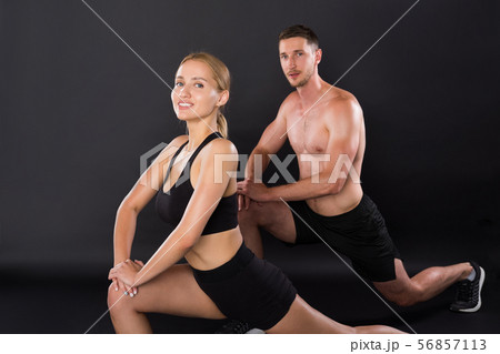 Athletic young couple doing stretching legs exercises together on the black background. 56857113