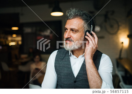Mature man with headphones at the table in a cafe, using laptop. 56857115