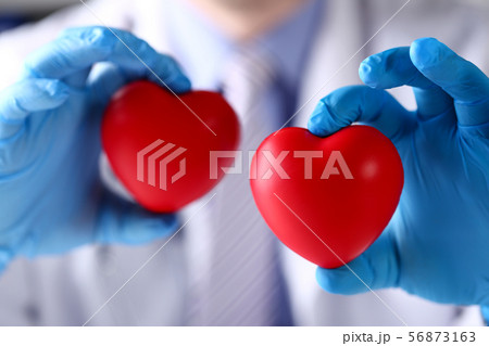 Surgeon in blue gloves showing two red toy hearts 56873163