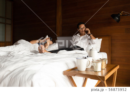 Coffee set with businessman and his wife using cell phone and laptop in bed. 56873952