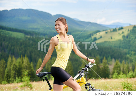 Attractive female cyclist with yellow mountain bicycle, enjoying sunny day in the mountains 56874590
