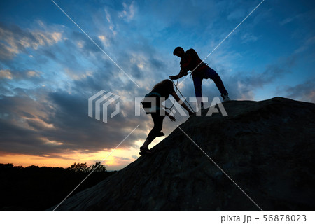 Young man and woman in the mountains. Woman with a rope engaged in rock climbing with man helping Young man and woman in the mountains. Woman with a rope engaged in rock climbing with man helping 56878023