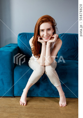Redhead woman sitting on the blue couch at home. 56878820