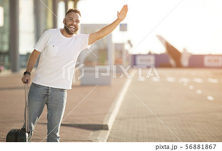 Catch taxi. Young man standing near airport, raising hand Catch taxi. Young man standing near airport, raising hand 56881867