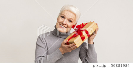 Elderly lady holding gift box with red ribbon bow 56881984