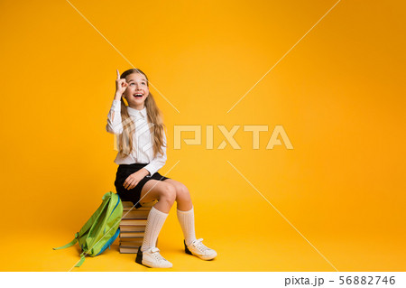 Clever Elementary School Girl Pointing Finger Up Sitting On Stack Of Books 56882746
