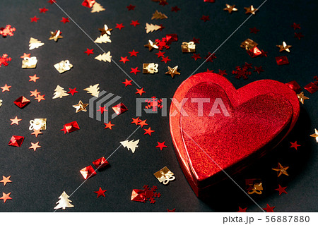Red heart-shaped gift box and festive golden confetti on a black background 56887880